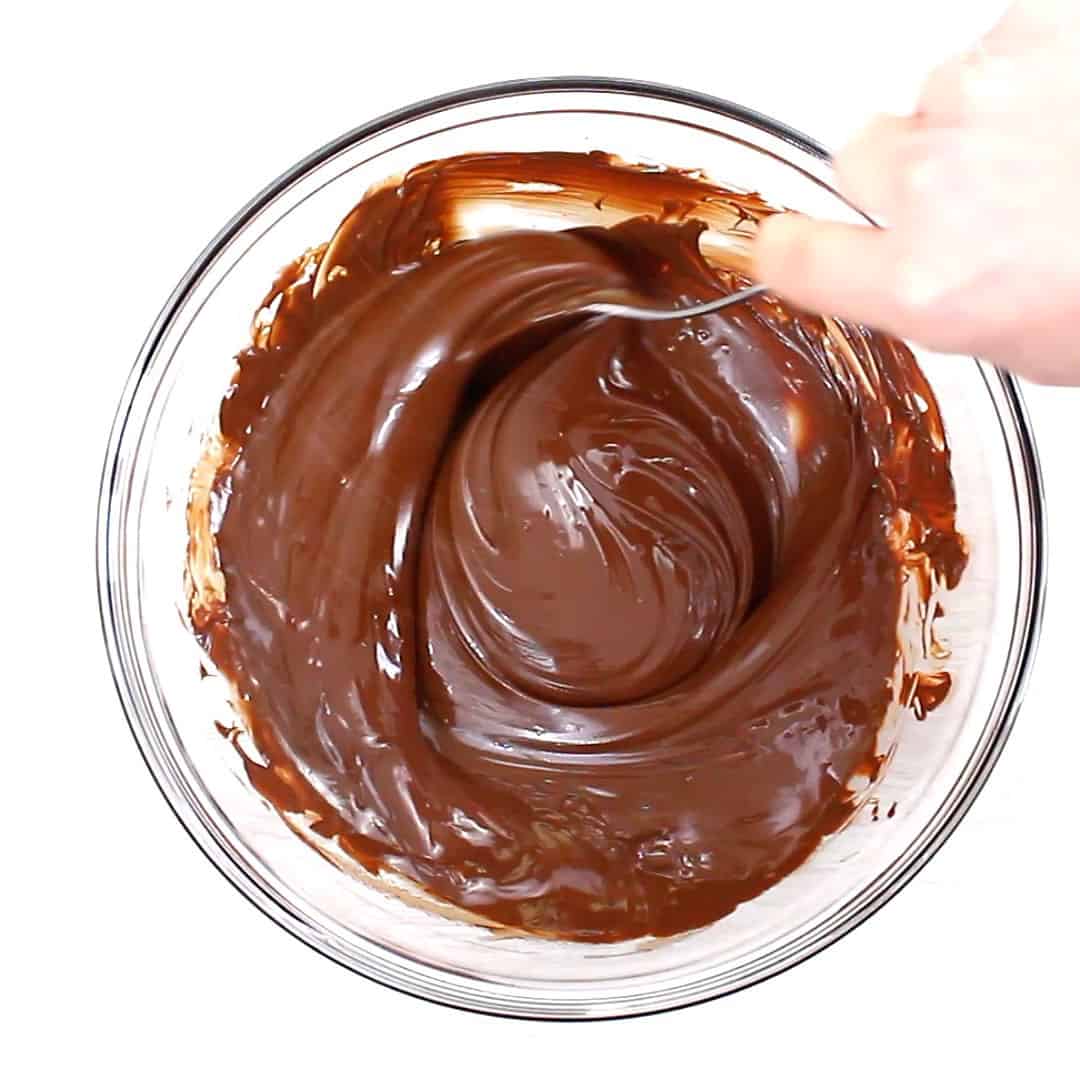 Hand stirring melted chocolate in mixing bowl to prepare chocolate base for almond bark