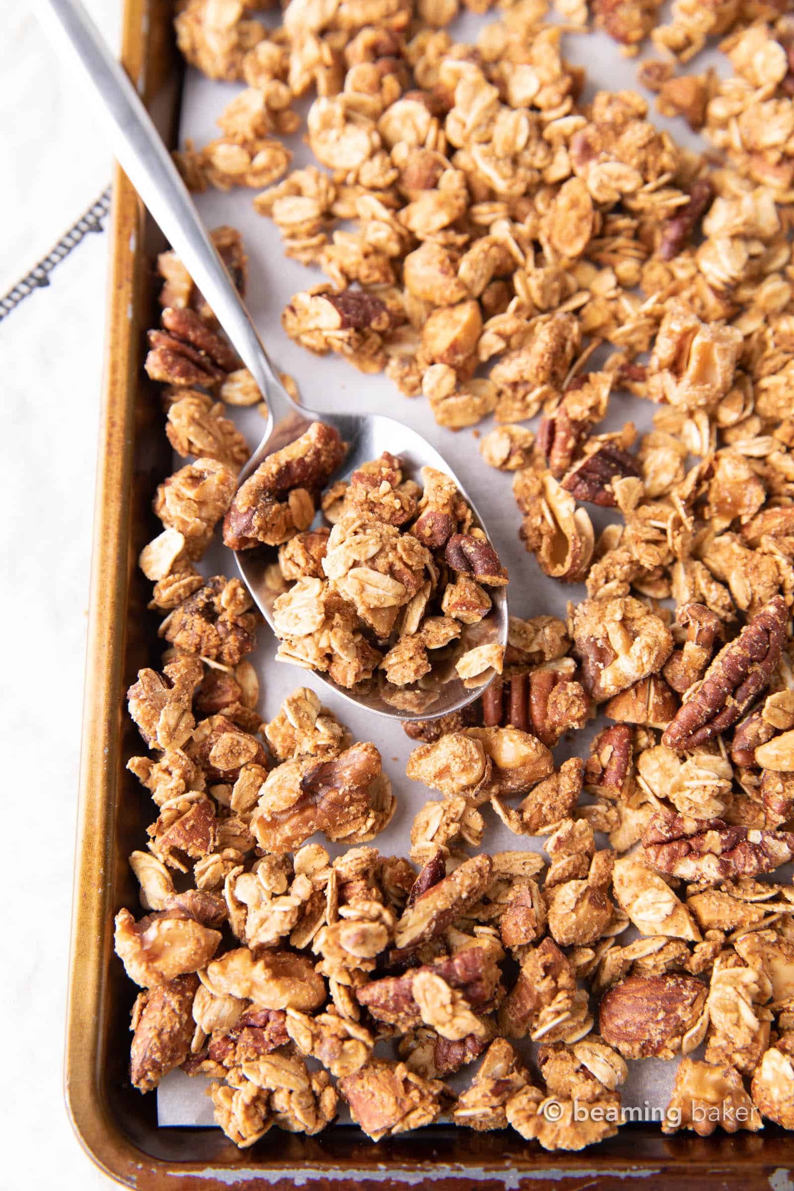 A spoonful of gluten free granola sitting on a baking sheet surrounded in granola.