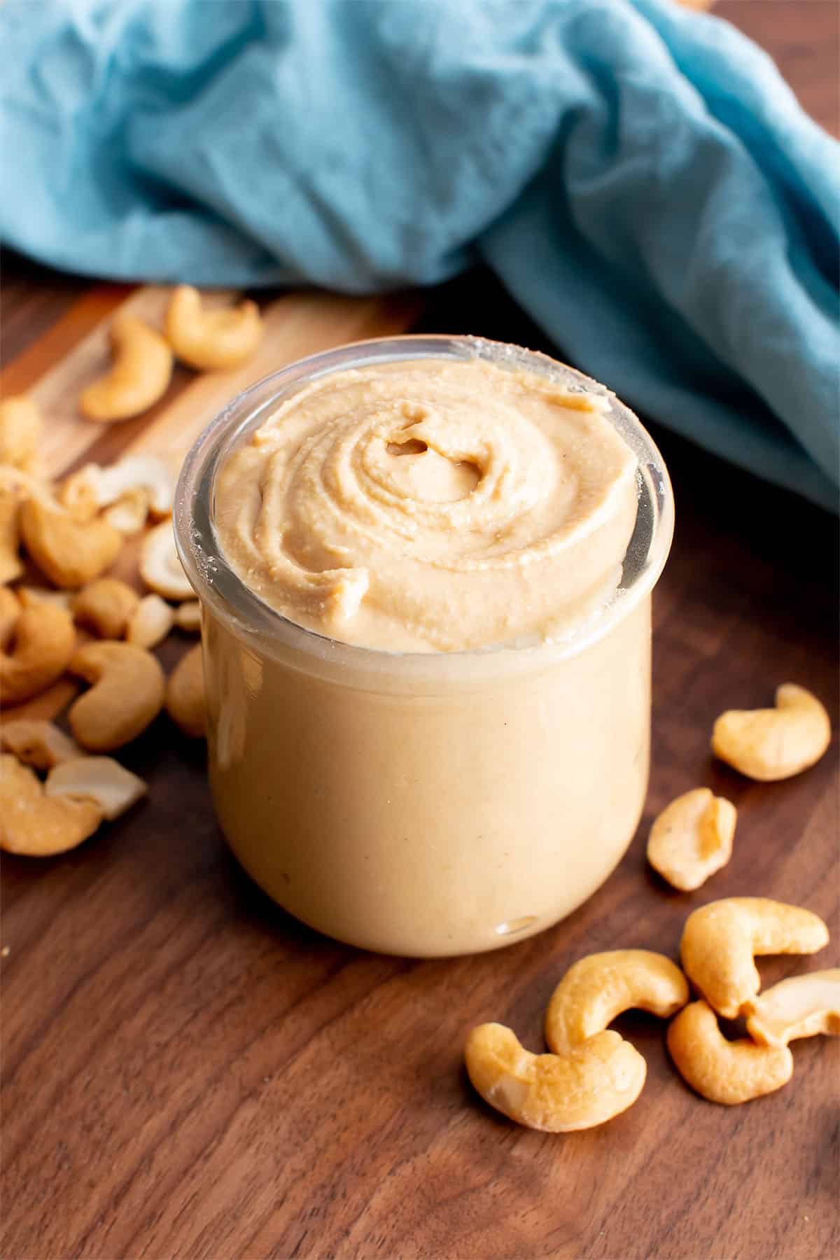 Cashew butter in a jar with cashews on a wooden table