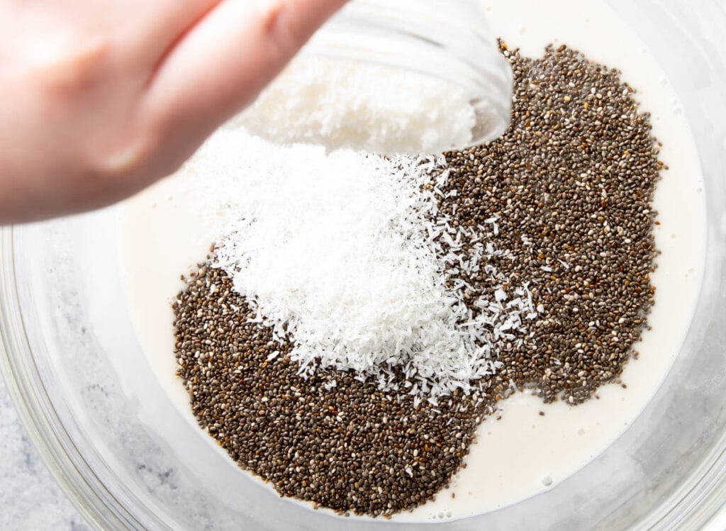 Close up photo showing shredded coconut being poured over chia pudding mixture