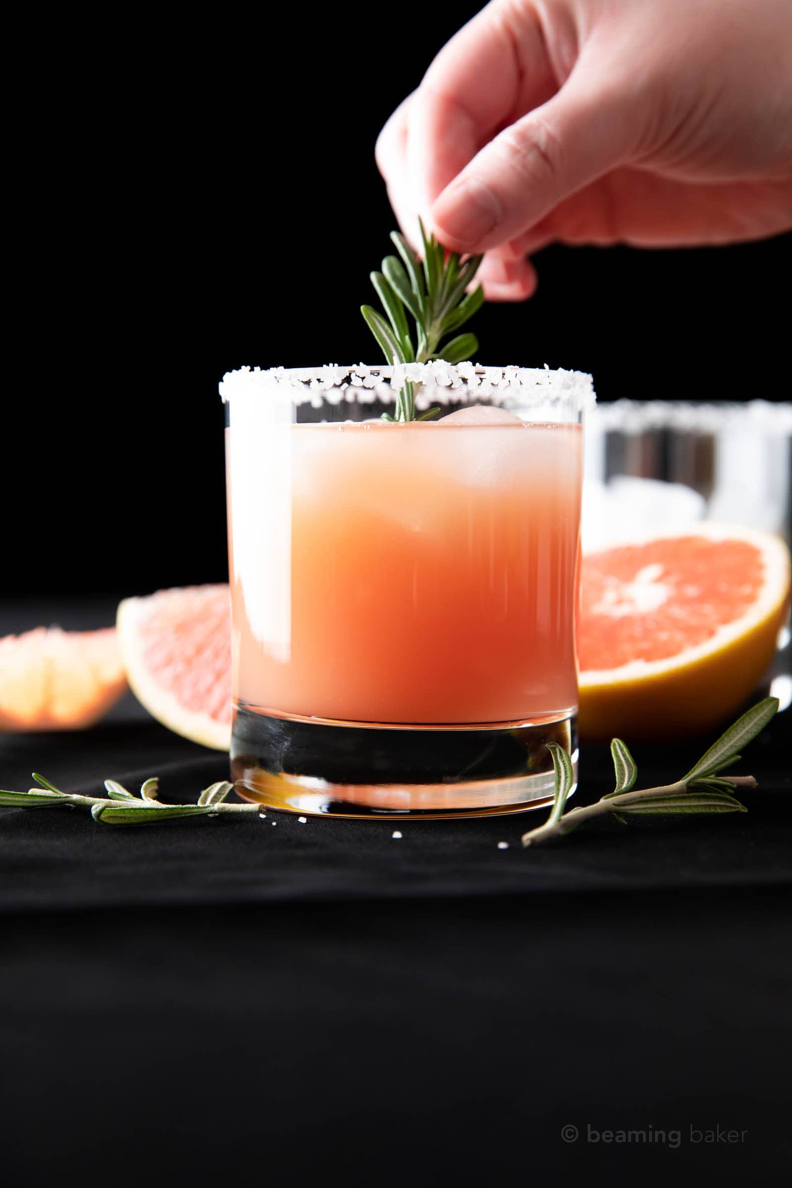 hand dropping rosemary garnish into a glass filled with salty dog cocktail