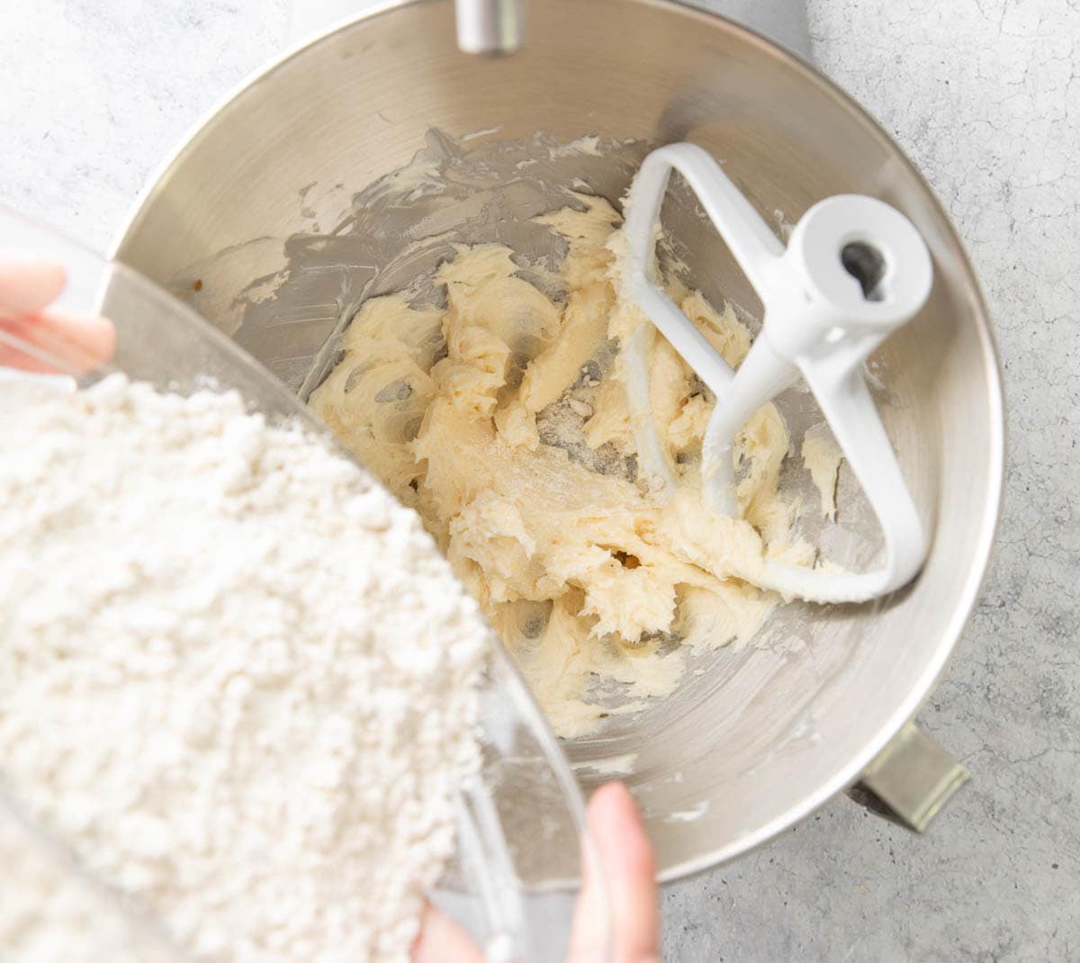Adding the dry flour mixture into the stand mixer filled with creamed butter to create cookie dough